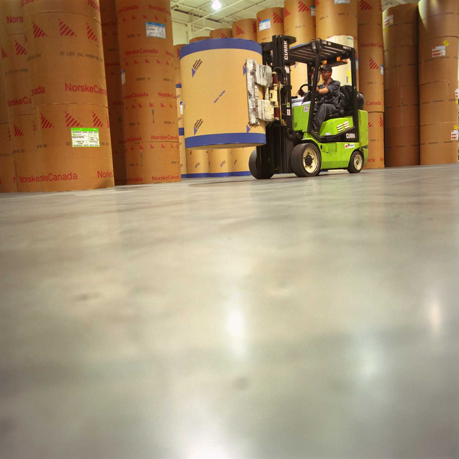 A man is driving a forklift with printing materials over the shiny concrete surface of TC Transcontinental's floor.