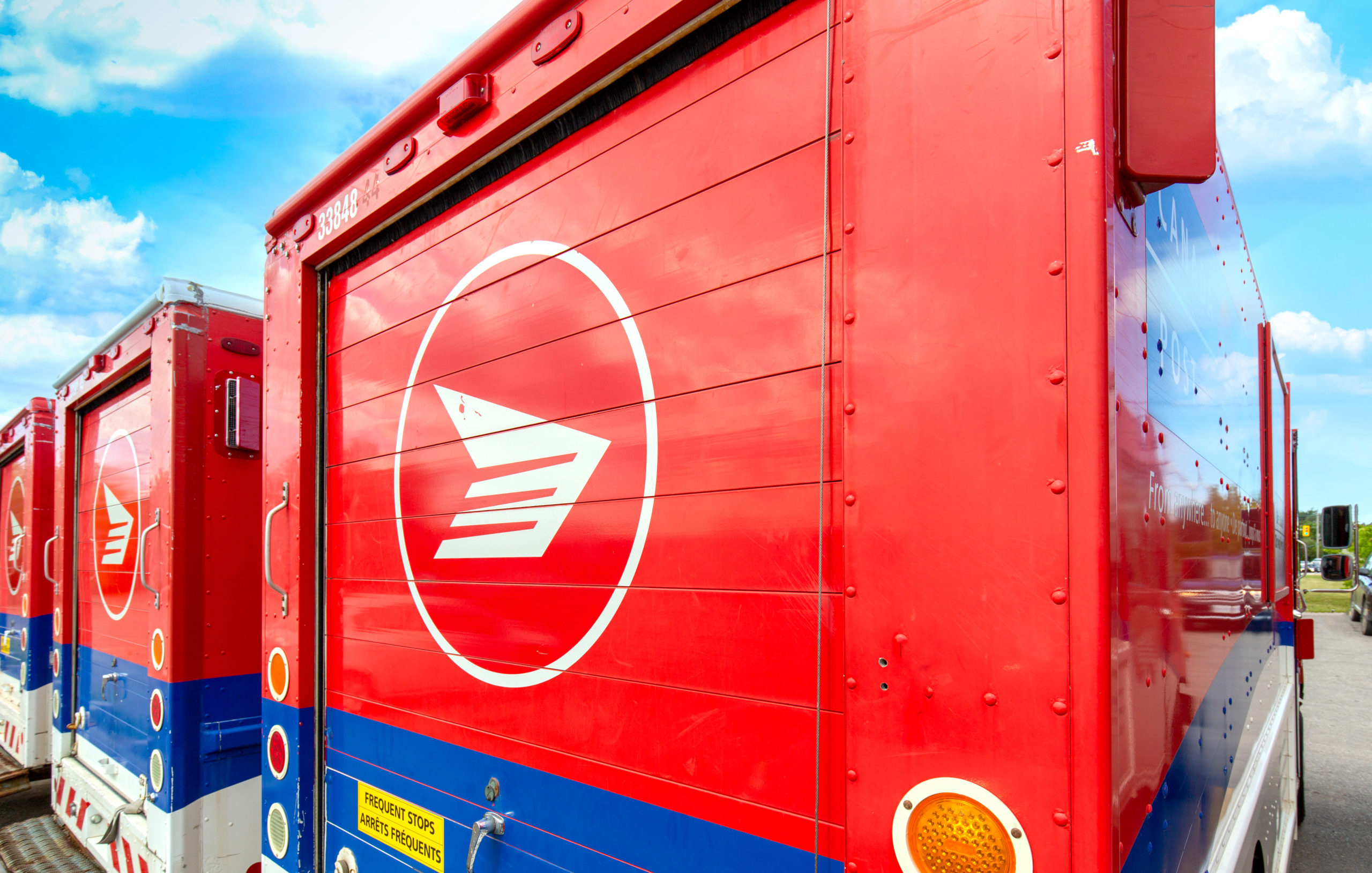 Canada Post trucks are parked under a bright blue sky.